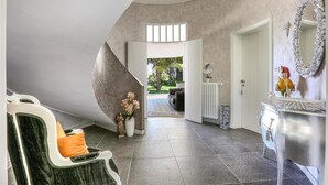 Een modern interieur met een gebogen plafond, een zithoek met een fauteuil en een witte dressoir en spiegel.