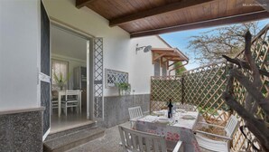 Une terrasse avec une table dressée pour deux personnes, entourée de chaises blanches, et une pergola en bois au-dessus.