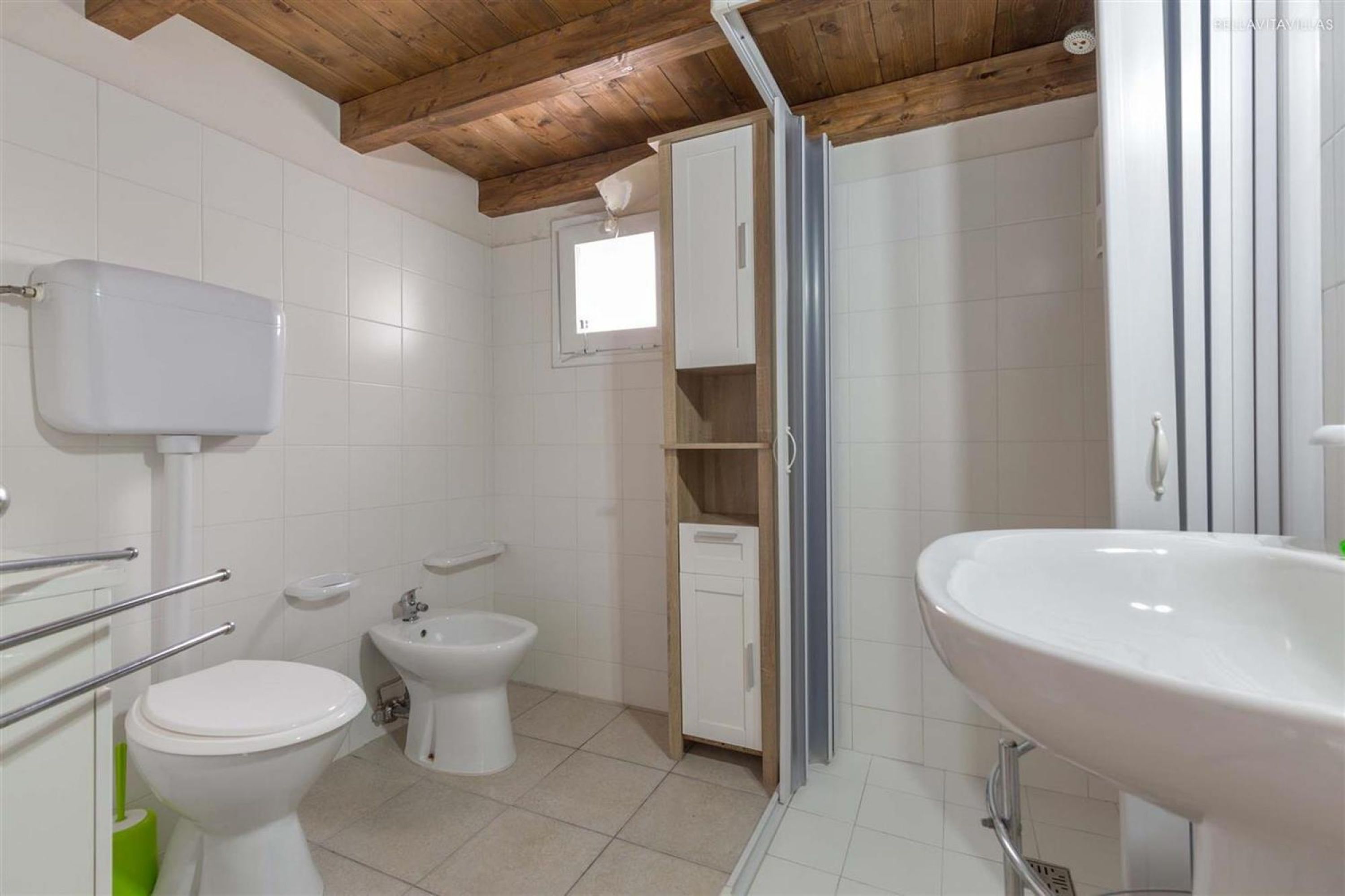 Een badkamer met toilet, bidet, wastafel en een kastje.