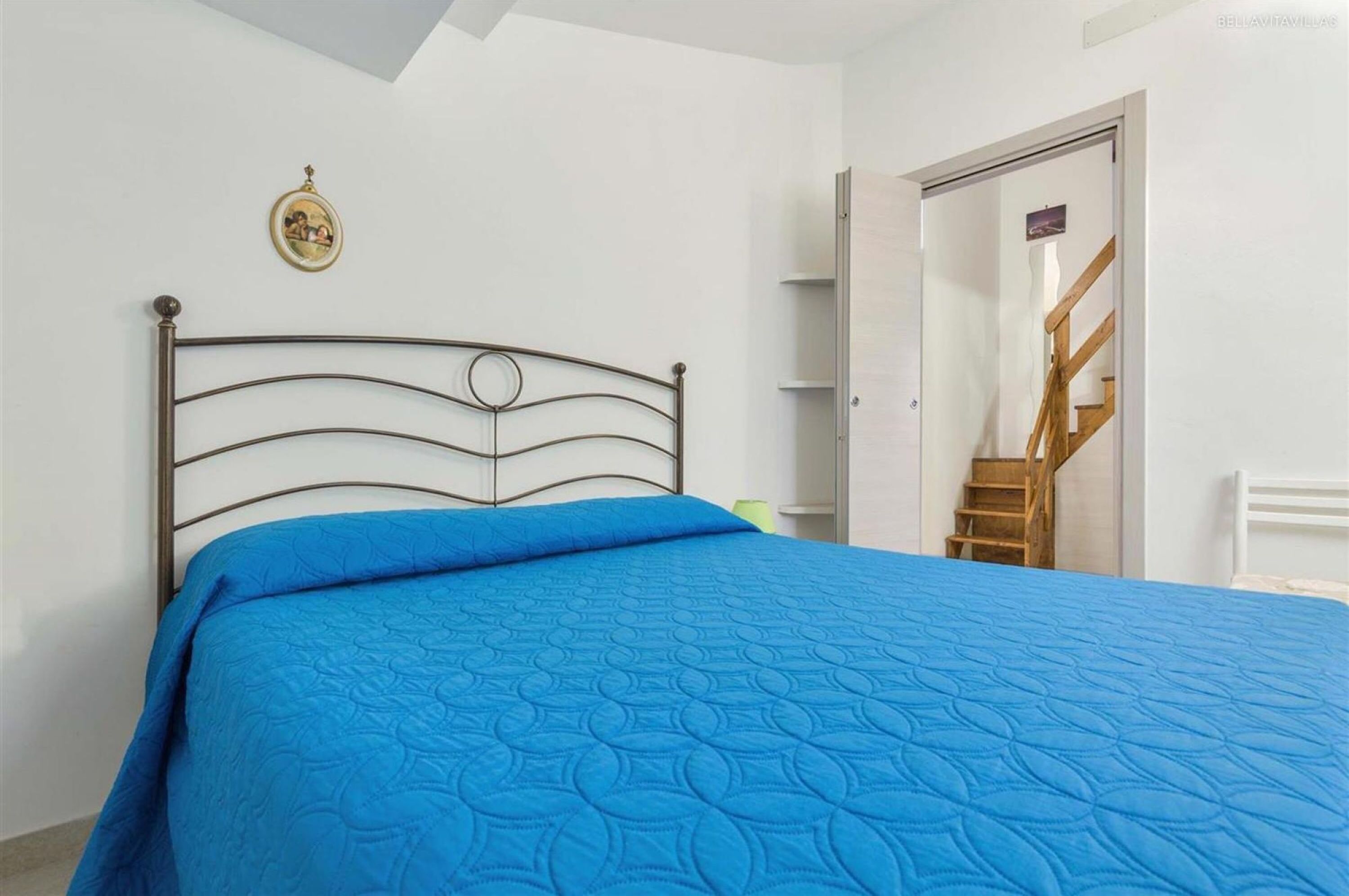 Un dormitorio con una cama, una escalera de madera y una pared blanca con un marco de cuadro.
