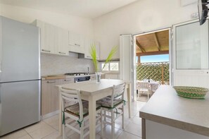 A modern kitchen with white cabinets, a stainless steel refrigerator, and a dining area with a table and chairs. - 2337 Bilo Imma A by Barbarhouse (Porto Cesareo)