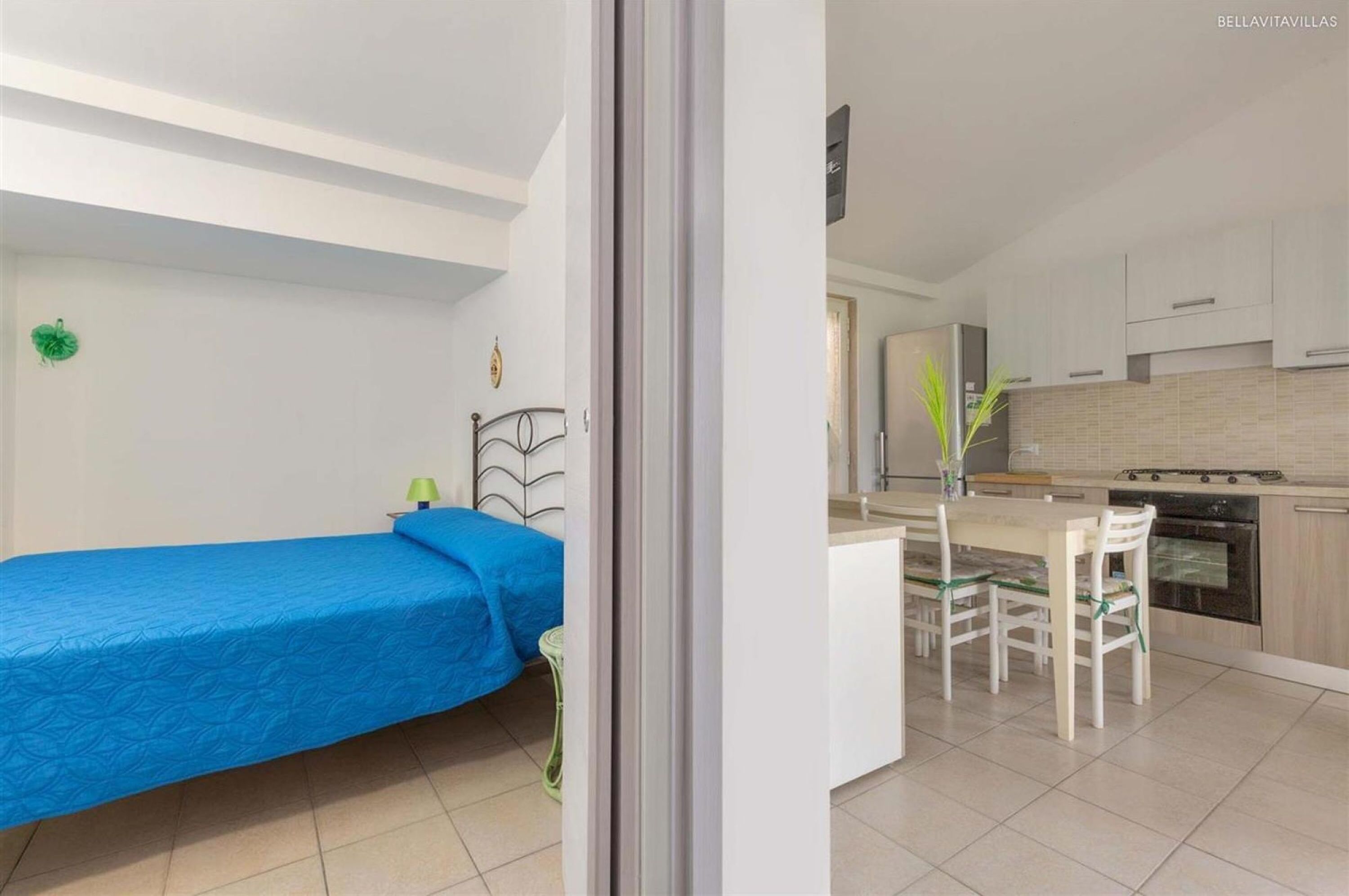 A compact room with a single bed, a small table with chairs, and a kitchenette.