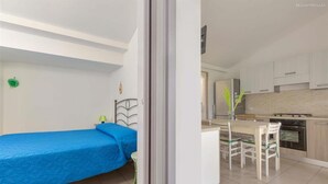 Une chambre de taille modeste comprenant un lit simple, une petite table avec des chaises et un coin cuisine.