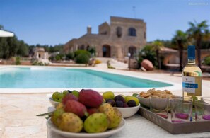 Ein Tisch am Pool mit einer Flasche Weißwein, Obstschalen und Gläsern.