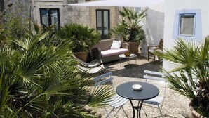 An outdoor patio with a sofa, chairs, and a table. There are potted plants and a building with a stone facade in the background. - 574 Loft nel Centro Storico di Presicce (Presicce-Acquarica)