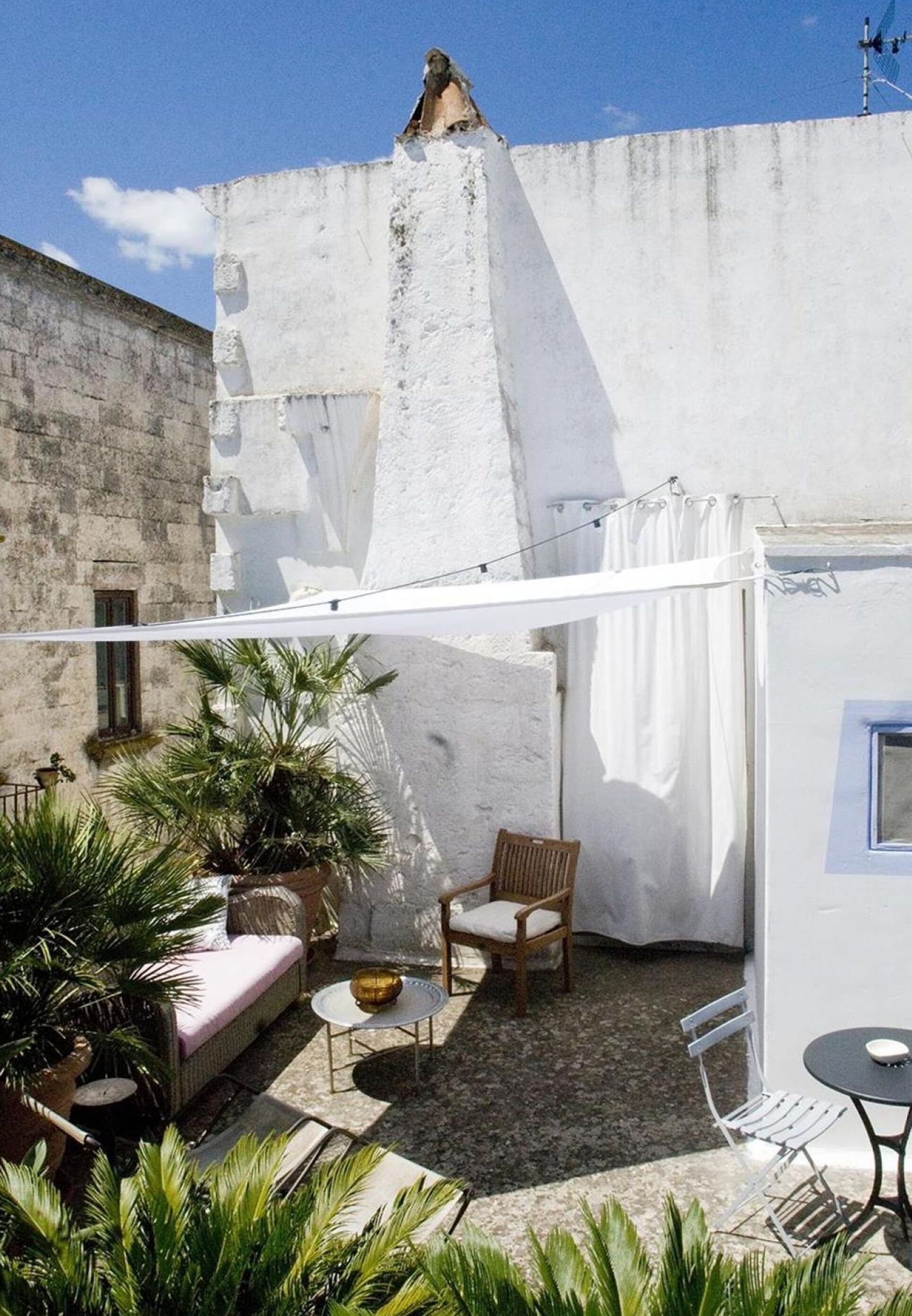 A courtyard with a white wall, a wooden chair, a small table, and potted plants.