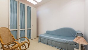 Une pièce avec un canapé bleu, un fauteuil en osier, une lampe et une fenêtre ornée de rideaux bleus.