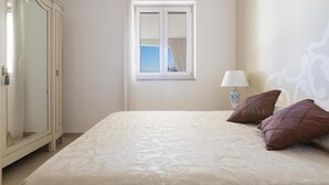 Une chambre à coucher avec un grand lit, une fenêtre avec des rideaux, une table de chevet avec une lampe et une armoire.