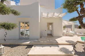 Una villa moderna con fachada blanca, puerta de cristal de entrada, zona de estar cubierta al aire libre y piscina.