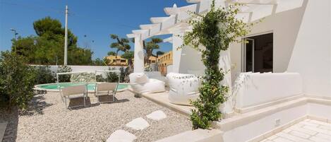 A modern outdoor patio with a pool, white furniture, and a pergola.