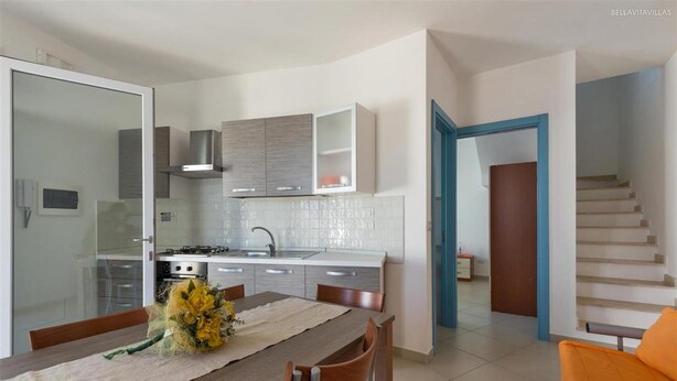 Una cucina moderna con zona pranzo, dotata di piano cottura integrato, pensili e una porta in vetro che dà su un'altra stanza.