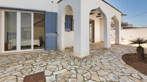 Un edificio moderno con un cortile in pietra, ampie porte scorrevoli in vetro e una zona esterna coperta con archi.