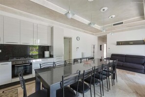 A modern kitchen with white cabinets, a dining table with chairs, and a dark-colored sofa in a living area. - 1695 Villa Albarosa in Ruffano (Ruffano)