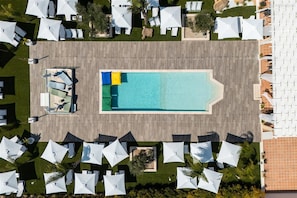 Vista aérea de un complejo turístico con una piscina rectangular, varias áreas de descanso con sombrillas y un césped bien cuidado.