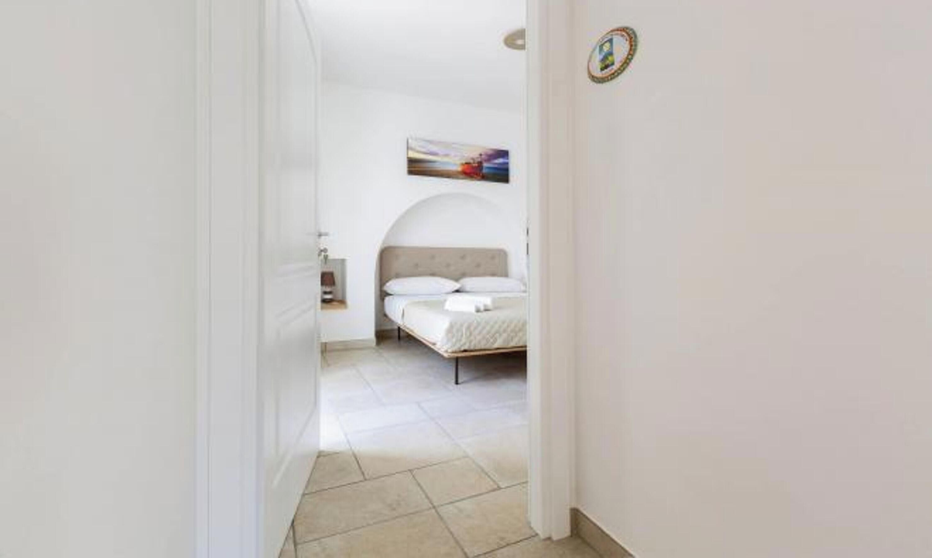 Un pasillo estrecho que conduce a un dormitorio con cama, mesita de noche y un cuadro en la pared.