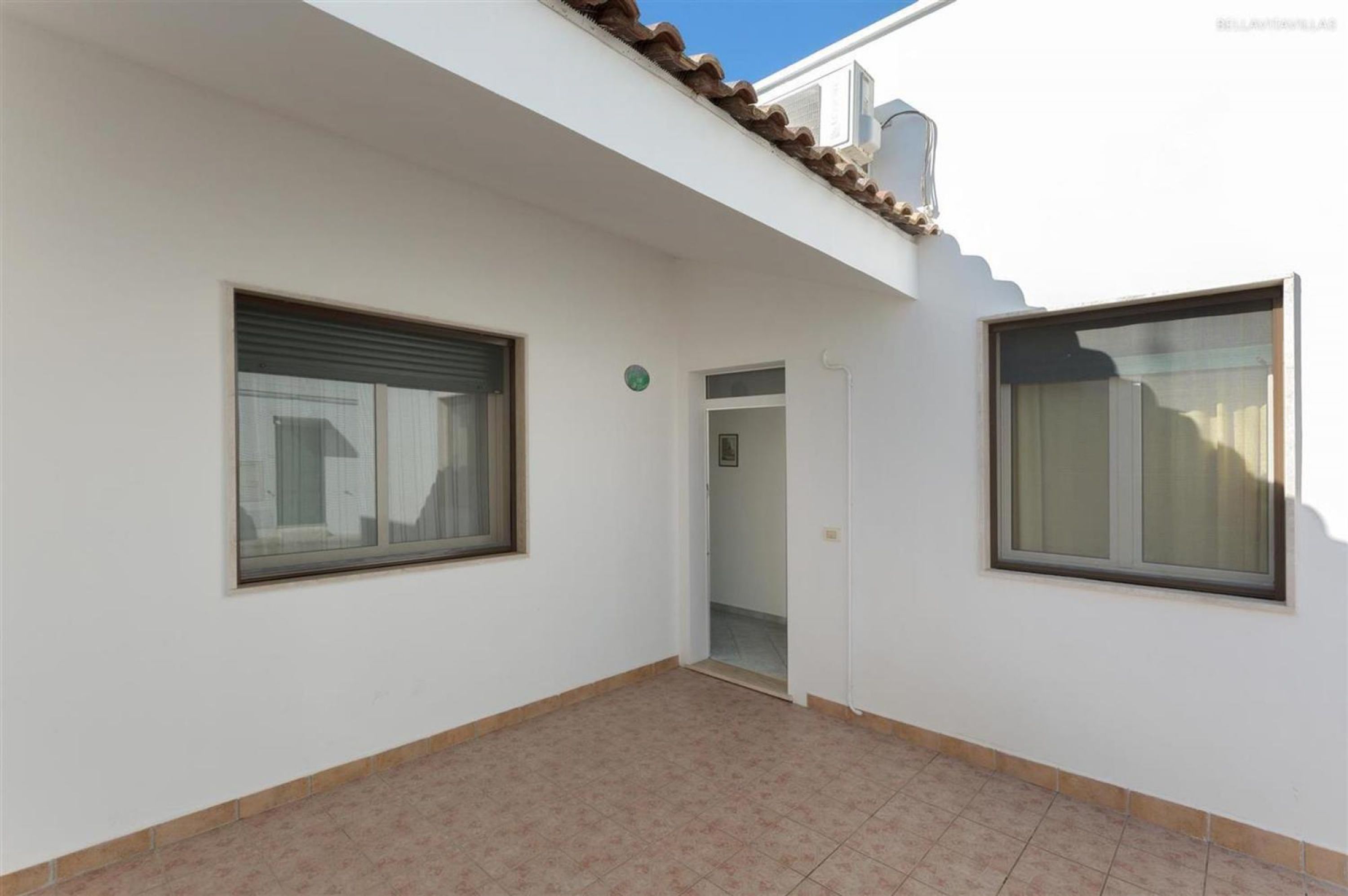 Un bâtiment blanc doté de deux grandes fenêtres et d’une porte donnant sur un espace intérieur.