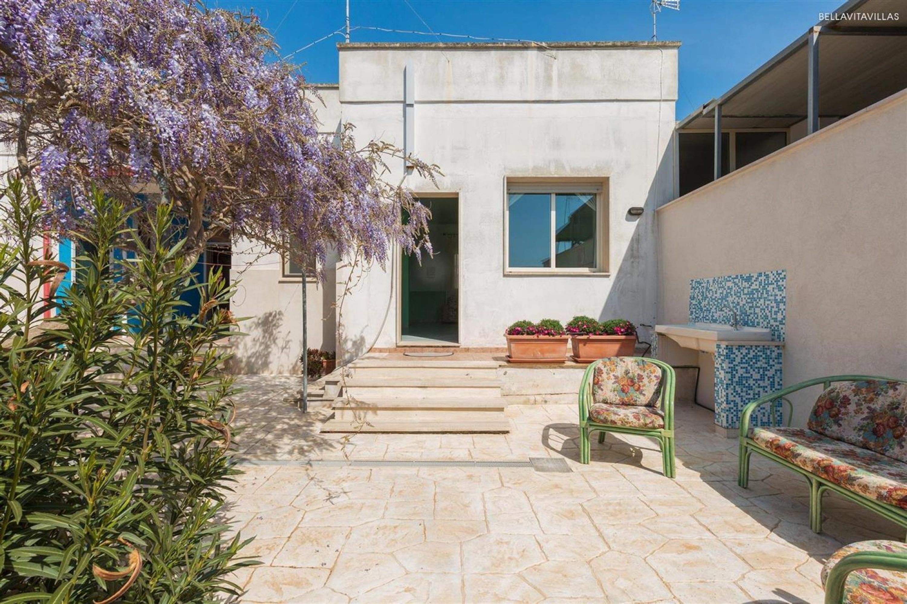A building with a white exterior, a door, a window, and a small balcony with a tiled table and chairs.