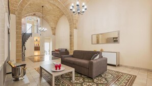 A spacious living area with a high arched ceiling, a chandelier, a sofa, a coffee table, and a decorative rug. - 2321 Dimora Terra Barone by Barbarhouse (Presicce-Acquarica)