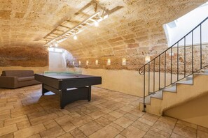 A spacious room with a pool table, a sofa, and a staircase leading to an upper level.