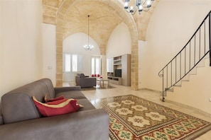 A spacious living area with a stone archway, a staircase, and a modern sofa with a red throw pillow.