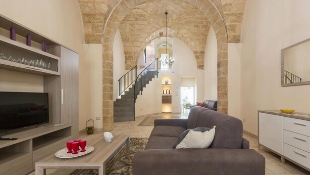 A spacious living area with a stone archway, a staircase leading to an upper level, a flat-screen TV, and a sofa. - 2321 Dimora Terra Barone by Barbarhouse (Presicce-Acquarica)