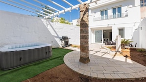 A modern outdoor patio with a hot tub, artificial grass, and a stone pillar. - 2321 Dimora Terra Barone by Barbarhouse (Presicce-Acquarica)