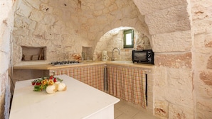 A kitchen with stone walls, a white countertop, a gas stove, a microwave, and a window with a green frame. - 2422 Il Trullo di Erna by Barbarhouse (Ostuni)