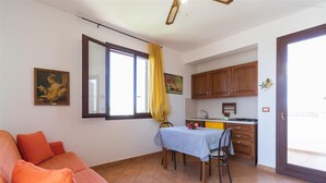 A living room with a sofa, a dining table with chairs, a kitchen area with cabinets, and a sliding glass door leading to an outdoor area. - 2406 Villa Cieloazzurro - Mono B by Barbarhouse (Nardò)