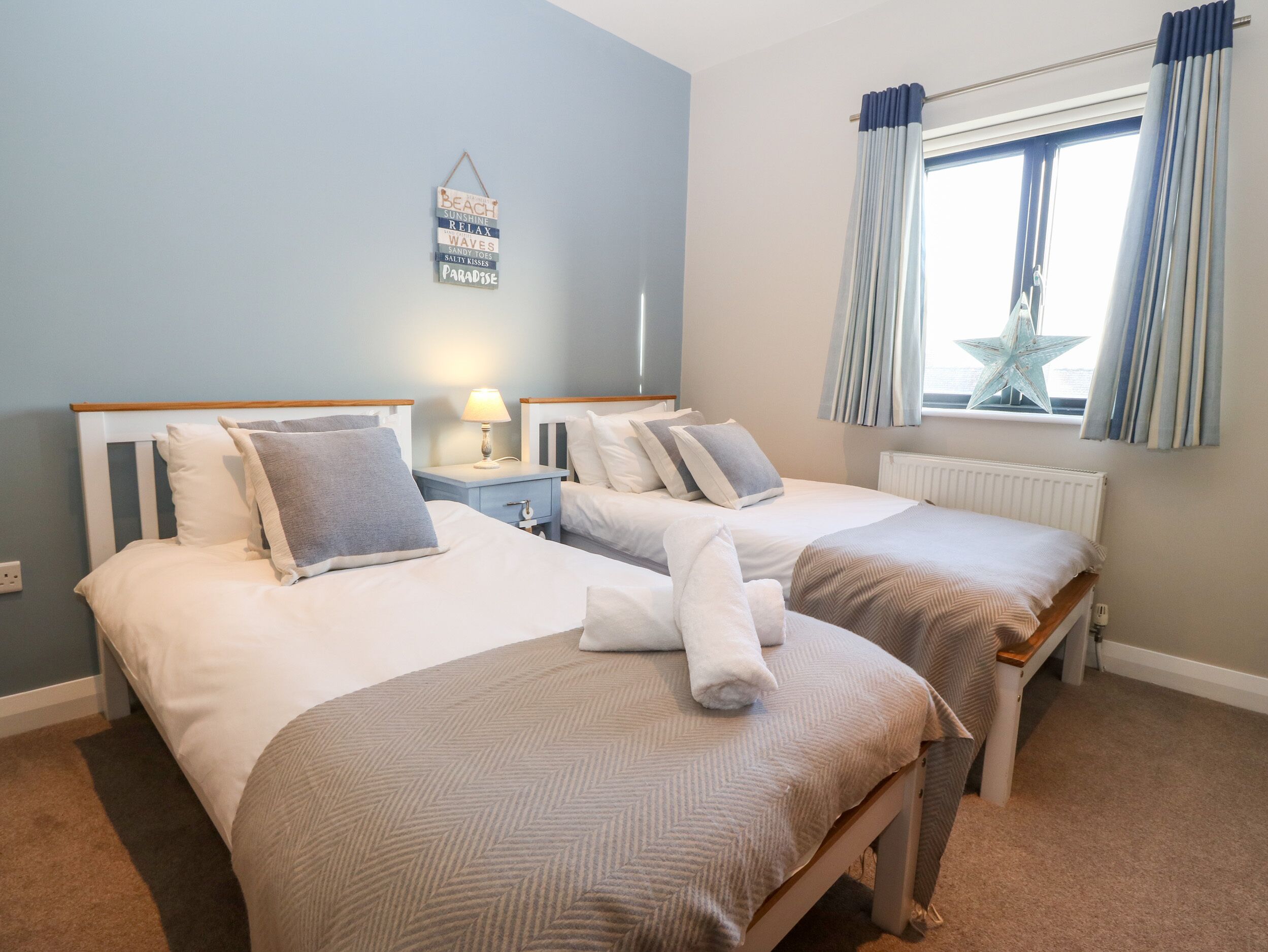Habitación de hotel con dos camas, una mesita de noche con lámpara, un adorno con forma de estrella y una ventana con cortinas.