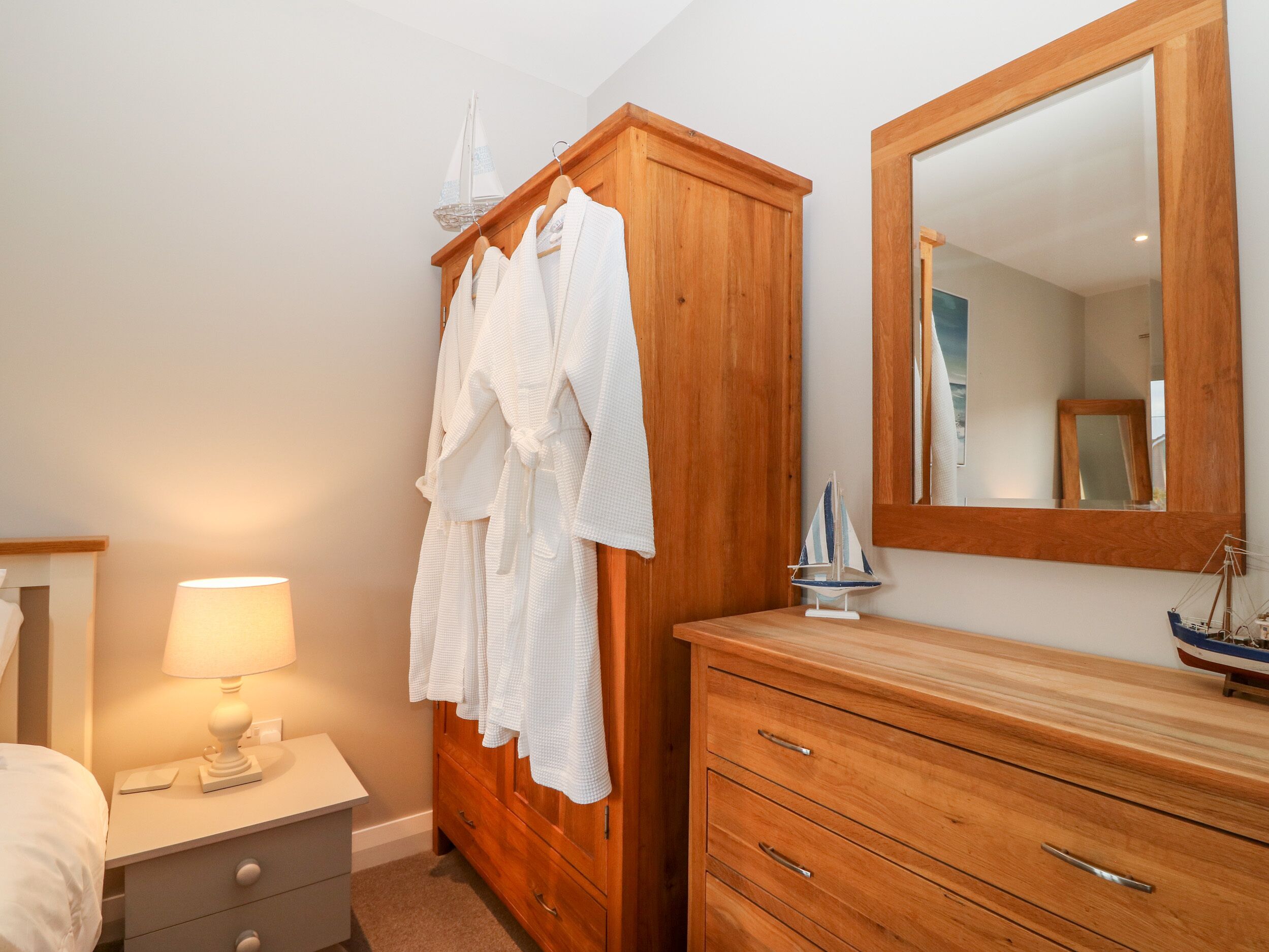 Une chambre à coucher avec une armoire en bois, une table de chevet avec une lampe et un miroir.