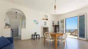 A spacious living area with a dining table, chairs, a sofa, and a balcony with a view.