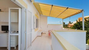 A balcony with a striped awning, a small table, and a chair. - 1091 Appartamento Cal Primo Piano (Ugento)
