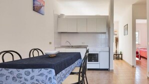 A compact kitchen with white cabinets, a stove, and a sink. There is a dining table with chairs and a decorative bowl. - 1091 Appartamento Cal Primo Piano (Ugento)