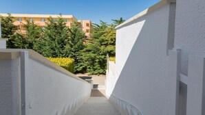 A narrow, white-walled stairway leading to a balcony with a view of a residential building and greenery. - 1091 Appartamento Cal Primo Piano (Ugento)