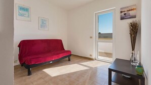 A room with a red sofa, a small table with a vase, and a door leading to a balcony. - 1091 Appartamento Cal Primo Piano (Ugento)