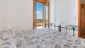 A bedroom with a bed, a chair, and a view of the sea through an open door. - 1132 Attico Isola dei Conigli (Porto Cesareo)