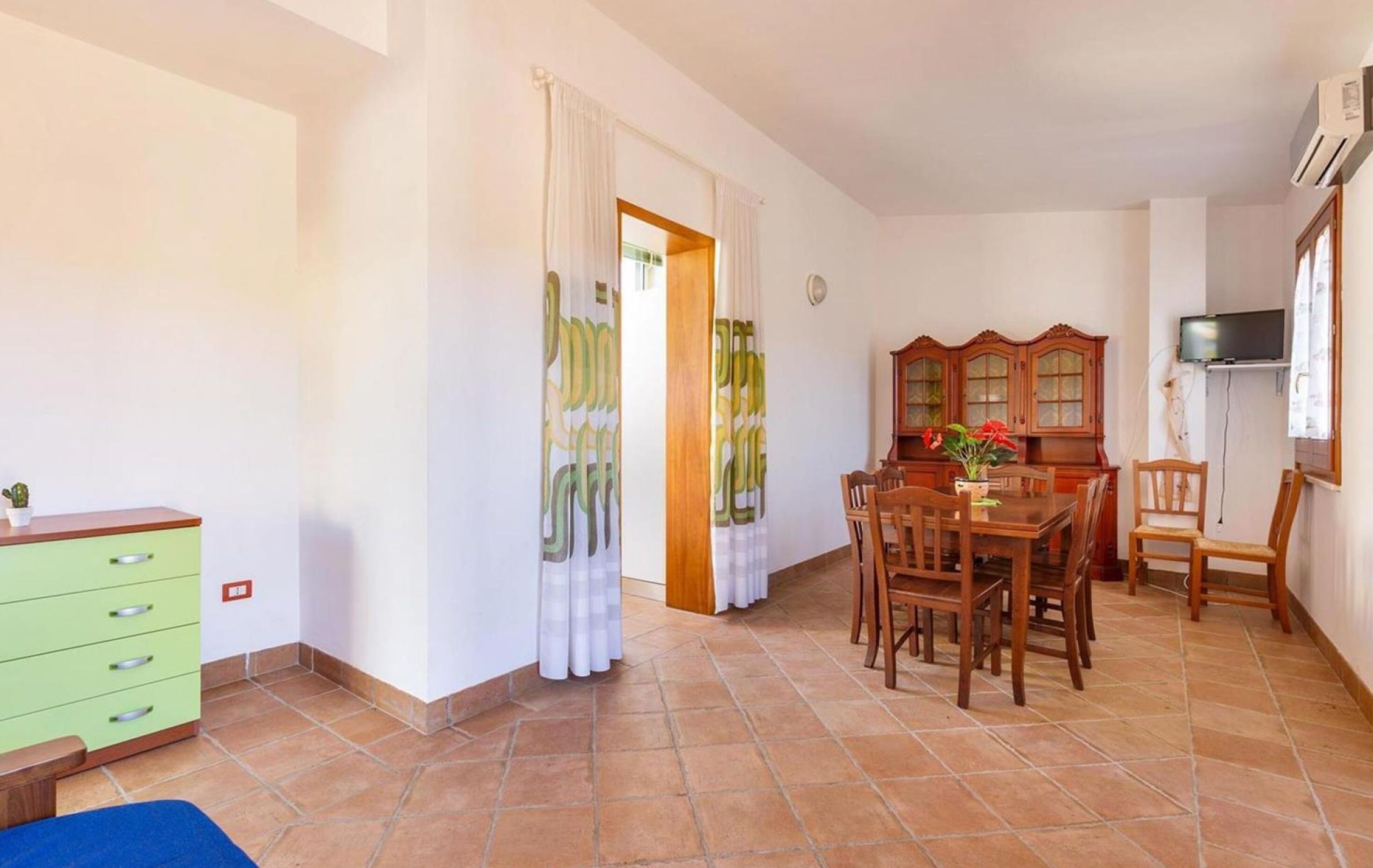 A room with a dining table, chairs, a TV, and a cabinet.