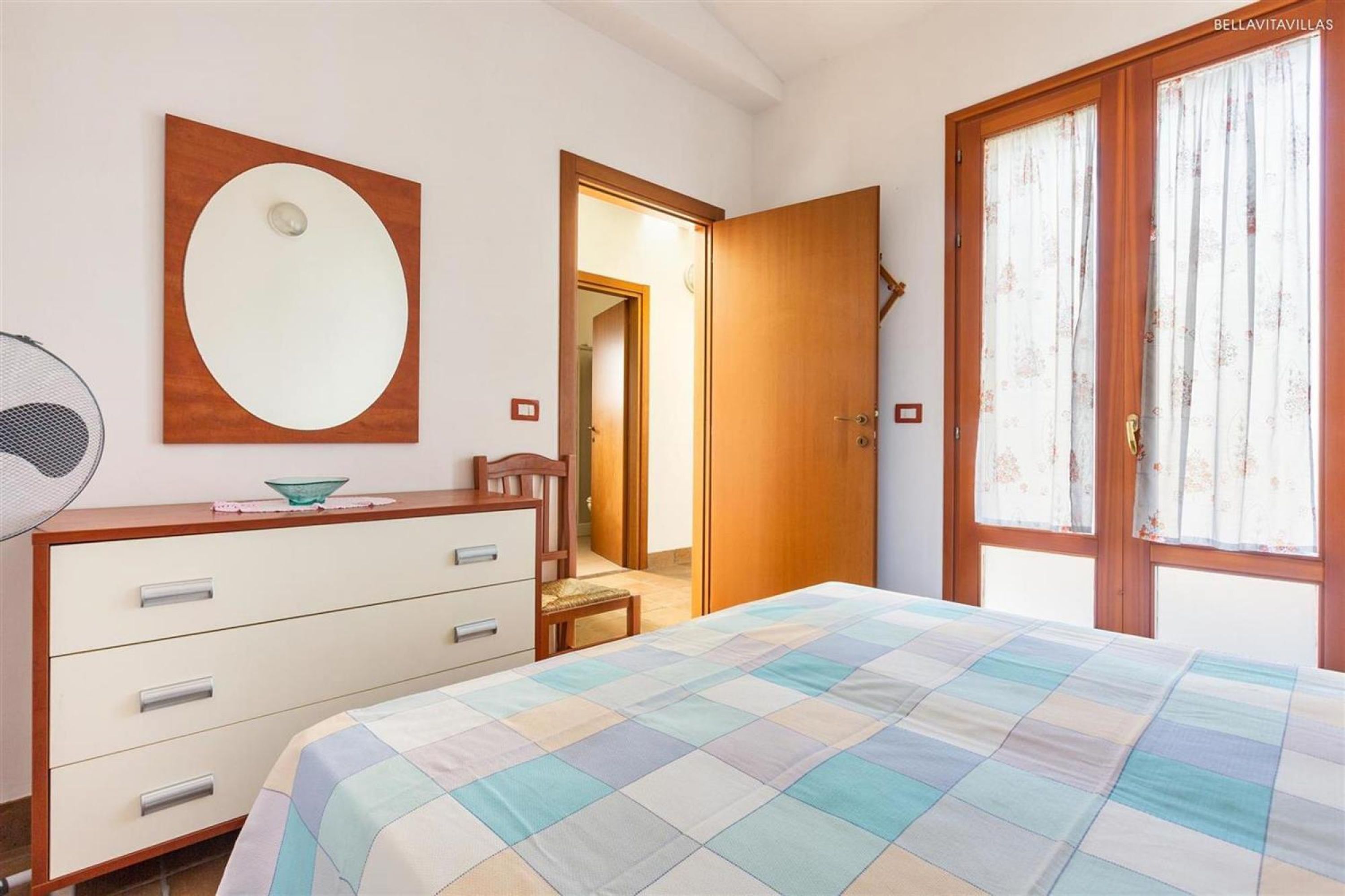 A bedroom with a bed, a dresser, a mirror, and a window with curtains.