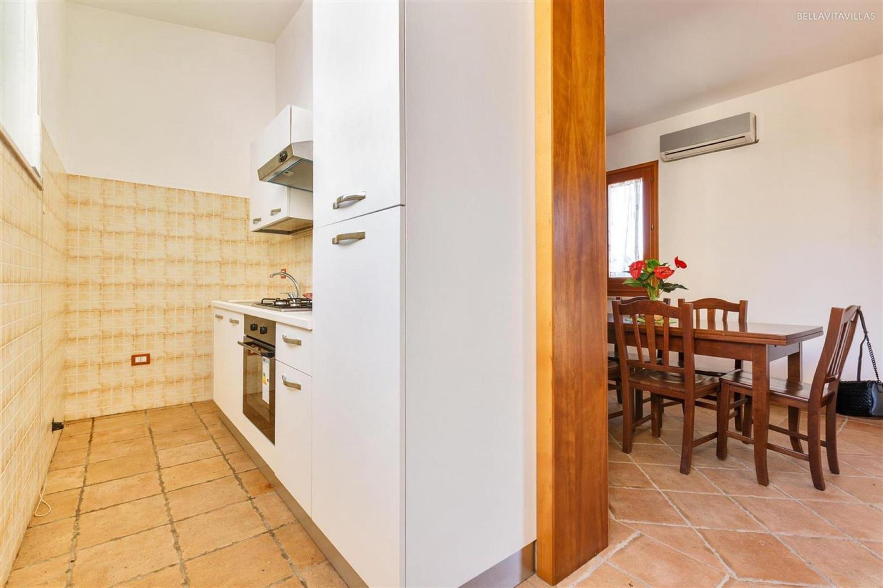 A compact kitchen with white cabinets, a stove, and a dining area with wooden chairs and a table.