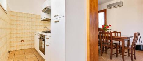 A compact kitchen with white cabinets, a stove, and a dining area with wooden chairs and a table.