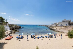 Una spiaggia con acque cristalline blu, un litorale roccioso e un edificio con facciata bianca.