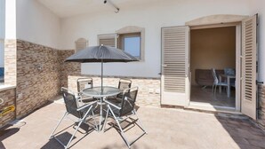 An outdoor patio with a round table and chairs, a black umbrella, and a sliding glass door leading to an interior space. - 2300 Villino Vanessa (Porto Cesareo)