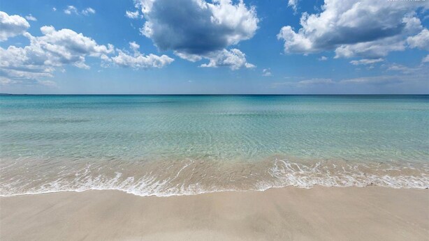 A beach with clear turquoise water and a sandy shore under a partly cloudy sky. - 2300 Villino Vanessa (Porto Cesareo)