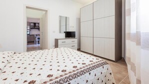 A bedroom with a bed, a wardrobe, a television on a stand, and a mirror on the wall. - 2300 Villino Vanessa (Porto Cesareo)