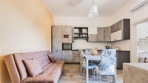 A modern kitchen with built-in appliances, a dining area with a table and chairs, and a sofa in a living area. - 2300 Villino Vanessa (Porto Cesareo)