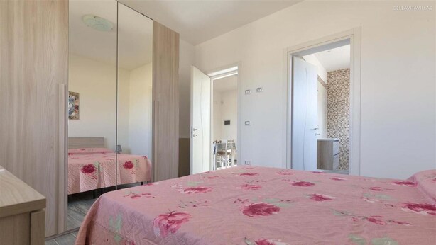 Ein Schlafzimmer mit Bett, Kleiderschrank und einem durchgegangenen Tür angedeuteten Badezimmer.