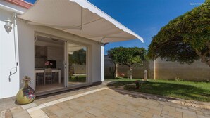 Ein überdachter Patio-Bereich mit Glastür, die zu einer Küche und einem Essbereich führt.