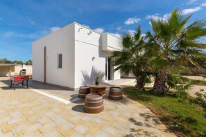 Un bâtiment moderne doté d’un toit plat, d’un petit patio avec une table et des chaises, et d’un palmier.