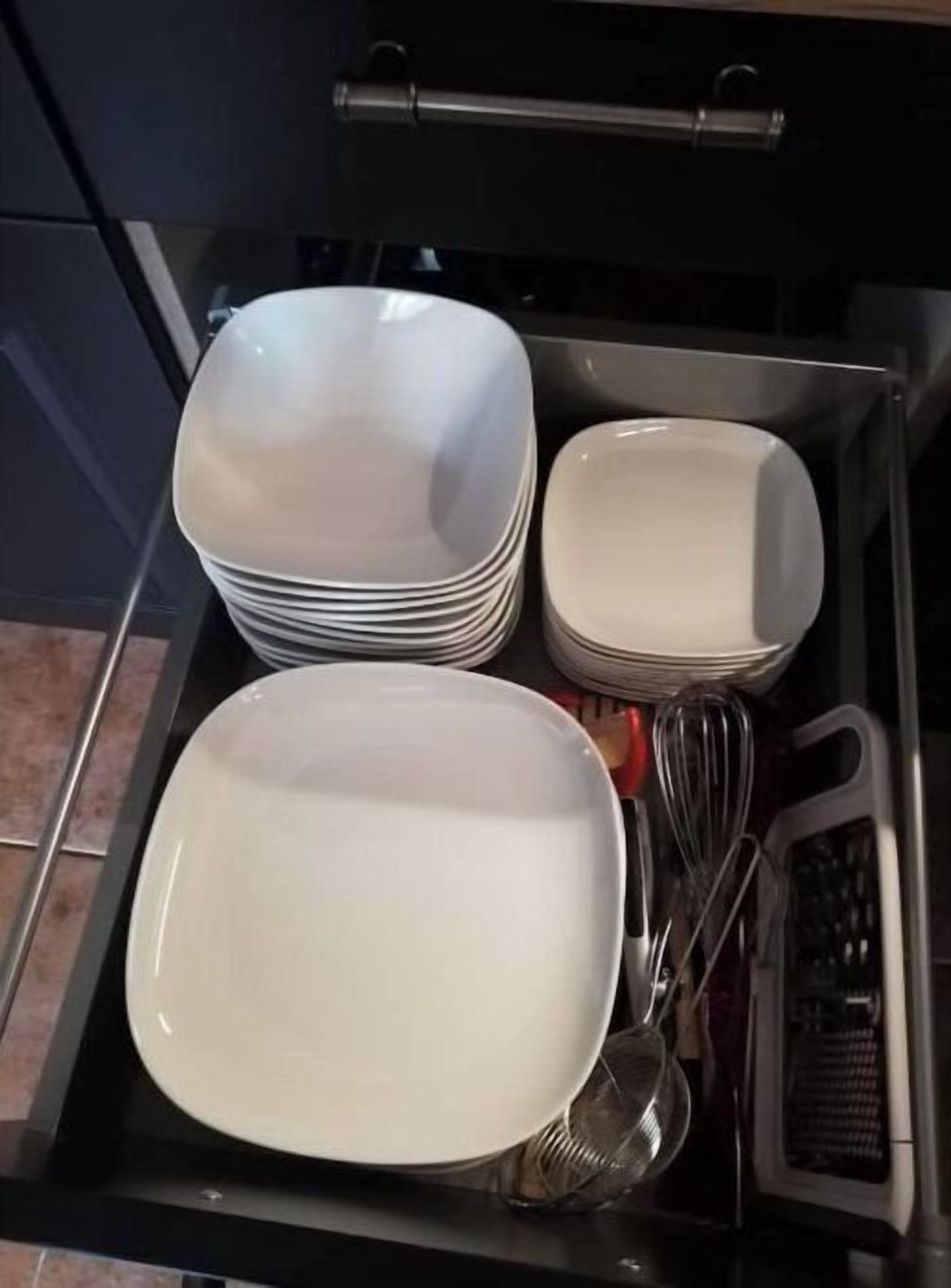 A kitchen drawer with stacked white plates and a whisk.