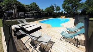 Ein Pool mit Holzterrasse, Liegestühlen und einer überdachten Sitzgelegenheit.